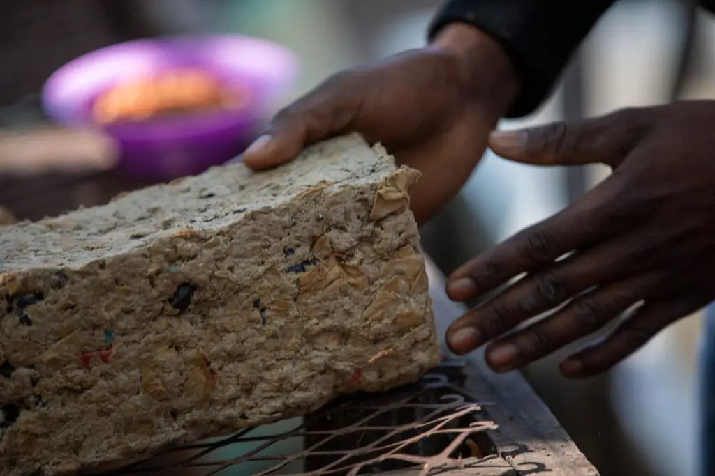 Hands placing a brick made from upcycled waste paper onto a drying rack